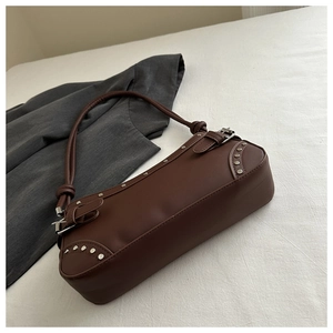 Close-up of a dark brown baguette shoulder bag with silver stud details and metal rivets