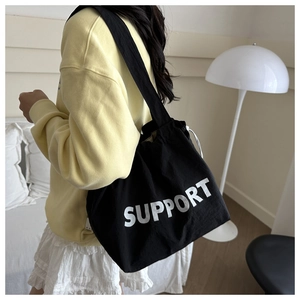 Détail d'un grand sac fourre-tout noir en toile avec imprimé SUPPORT porté par un mannequin