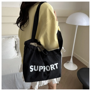 Détail du grand sac cabas en toile noire avec texte SUPPORT porté par un mannequin