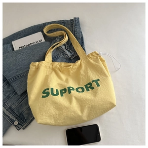Détail du sac cabas en toile jaune clair avec texte Support vert et cordon de serrage
