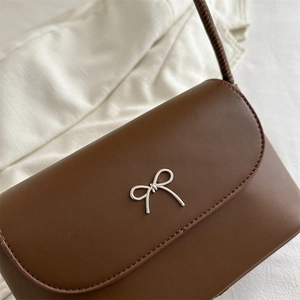 Brown faux leather shoulder bag with silver metal bow detail on a white background