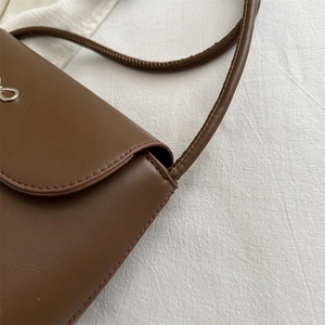 Brown leather shoulder bag with minimalist bow accent and silver ring hardware detail