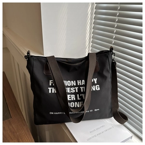 Detail shot of a black canvas tote bag with white lettering and brown strap by a window