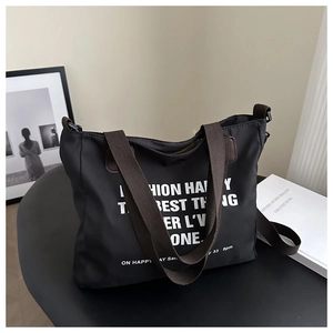 Detail of a black nylon tote bag with white typography and a brown wide textile strap