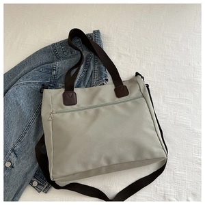 Detail of grey-green nylon tote bag featuring front zipper pocket and adjustable strap
