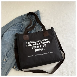 Detail of black canvas tote bag showing large white lettering and brown leather accents