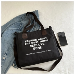 Detail of black canvas tote bag showing white typography and adjustable brown strap