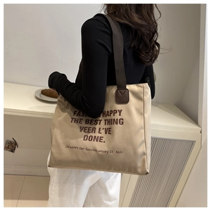 Side view of a large khaki canvas tote bag with brown lettering on a female model