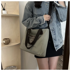 Gray-green canvas tote bag with adjustable brown strap shown in a mirror selfie