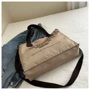 Detail view of canvas tote bag showing zipper closure, brown straps, and letter print