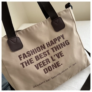 Detail of khaki canvas tote bag showing the brown letter print and reinforced leather handles