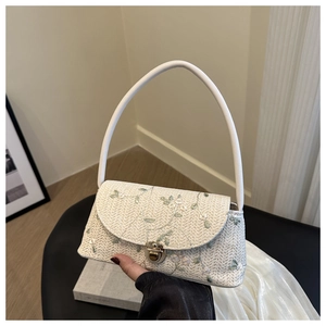 Detail of off-white straw bag featuring pink floral embroidery and gold metal clasp