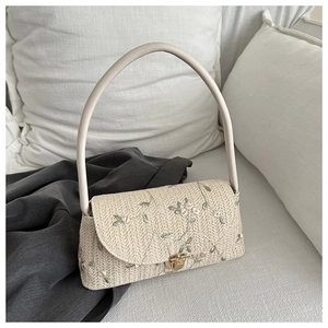 Detail of straw woven bag featuring delicate flower embroidery and gold metal turn-lock