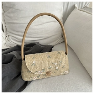 Detail of hand-woven straw bag featuring delicate floral embroidery and leather handle