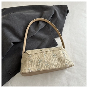 Detail of straw woven bag featuring delicate pink flower and green leaf embroidery
