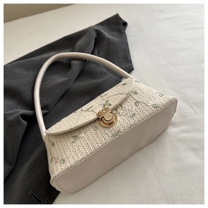Detail of floral lace embroidery and gold buckle on a woven straw underarm baguette bag