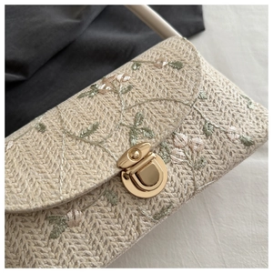 Detail of woven straw bag featuring floral embroidery and round gold metal clasp