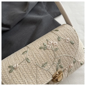 Detail of floral embroidery on beige woven straw bag with a gold metal twist lock