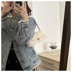 Mirror selfie showing a cream underarm bag with delicate pink and green floral embroidery