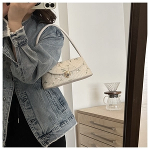 Detail of floral embroidery on a woven straw underarm bag with gold twist lock