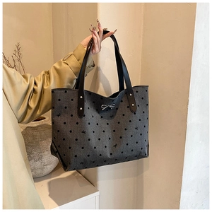 Close-up of gray polka dot tote bag with silver bow charm and black leather handles