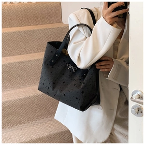 Close-up of black tote bag with star print, silver bow detail, and leather handles