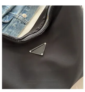 Close-up of black nylon tote with triangular metal logo and silver zipper detail