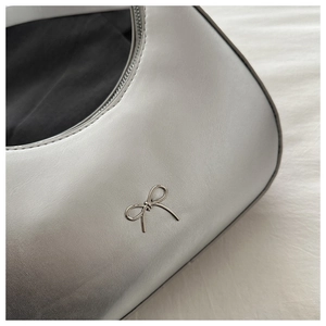 Detailed view of silver metallic bow logo on a minimalist textured leather shoulder bag