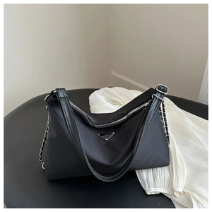 Macro detail of the smooth black nylon fabric and silver triangle logo on the tote bag
