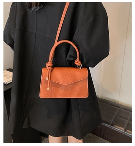 Detail of caramel orange pleated PU leather handbag with gold trim and knotted handle