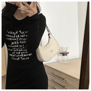 Detail of a white half-moon hobo bag with a metallic bow clasp shown in a mirror selfie
