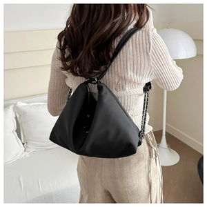 Detail shot of black triangular tote with silver metal chain strap on model