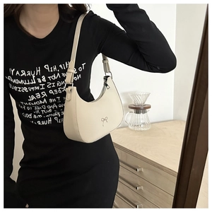 Close-up of cream-white half-moon hobo bag with metal bow detail and adjustable shoulder strap