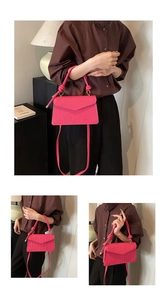 Detail of rose red textured crossbody bag with knotted handle and envelope flap design