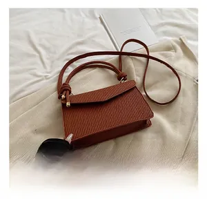 Detail of a brown pleated texture handbag with round metal buckle and crossbody strap