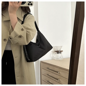 Detail of black nylon hobo bag with silver chain and metal plaque worn with a trench coat