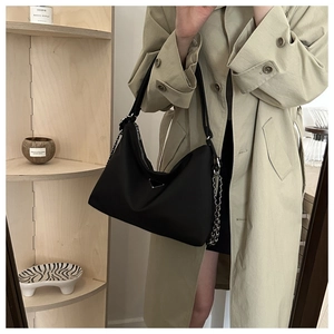 Detail of minimalist black nylon shoulder bag featuring iconic triangular metal logo plate