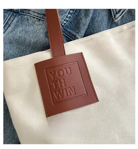 Close-up of canvas tote bag showing brown leather tag with embossed text and stitching