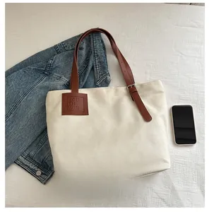 Canvas tote bag with leather strap and metal buckle shown next to a smartphone for scale