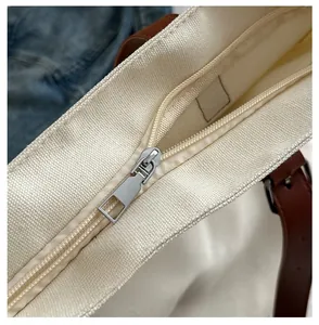 Detailed close-up of smooth silver metal zipper on off-white canvas tote bag with brown straps