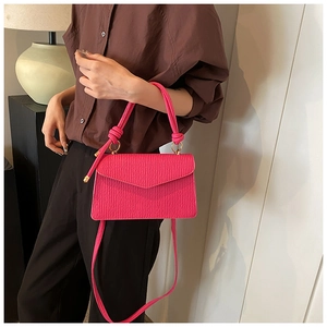 Detail of rose red textured handbag with gold ring hardware and woven knot handle
