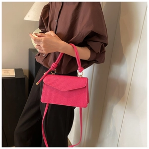 Detail showing magenta crossbody bag with vertical ripple texture and knotted top handle