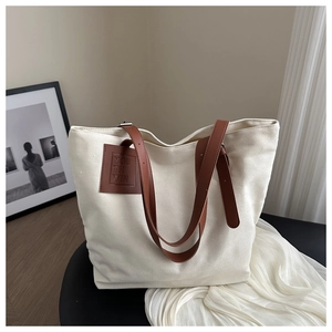 Detail of canvas tote bag with brown leather straps and embossed text on a chair