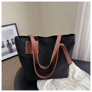 Detailed close-up of a large black canvas tote bag with brown synthetic leather handles