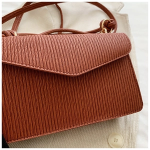 Close-up of pleated caramel leather handbag with vintage gold buckle and envelope flap