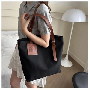 Detail of a large black canvas tote bag with brown leather straps and embossed patch