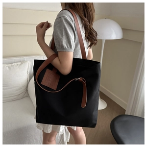 Detail of black canvas tote bag with brown leather straps shown on a female model