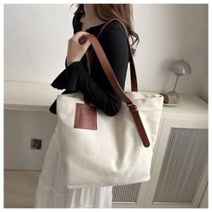 Detail of canvas tote bag featuring adjustable brown leather strap and logo patch