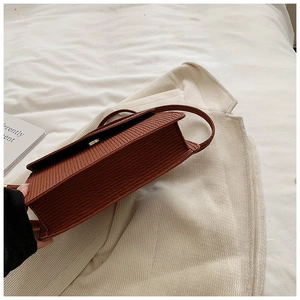 Close-up of brown crocodile embossed texture and gold metal lock on square handbag