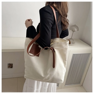 Detailed view of beige canvas tote bag with brown leather straps in a home setting